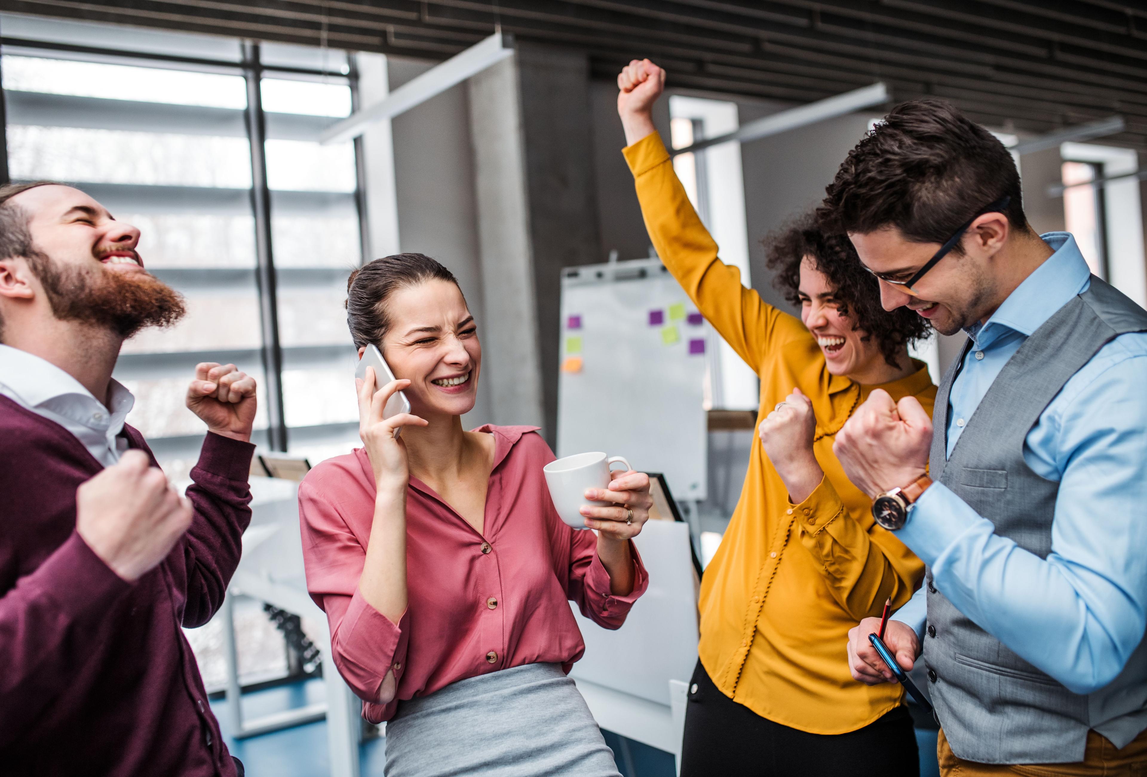 Group of coworkers celebrating together in an office, smiling and raising their fists.
