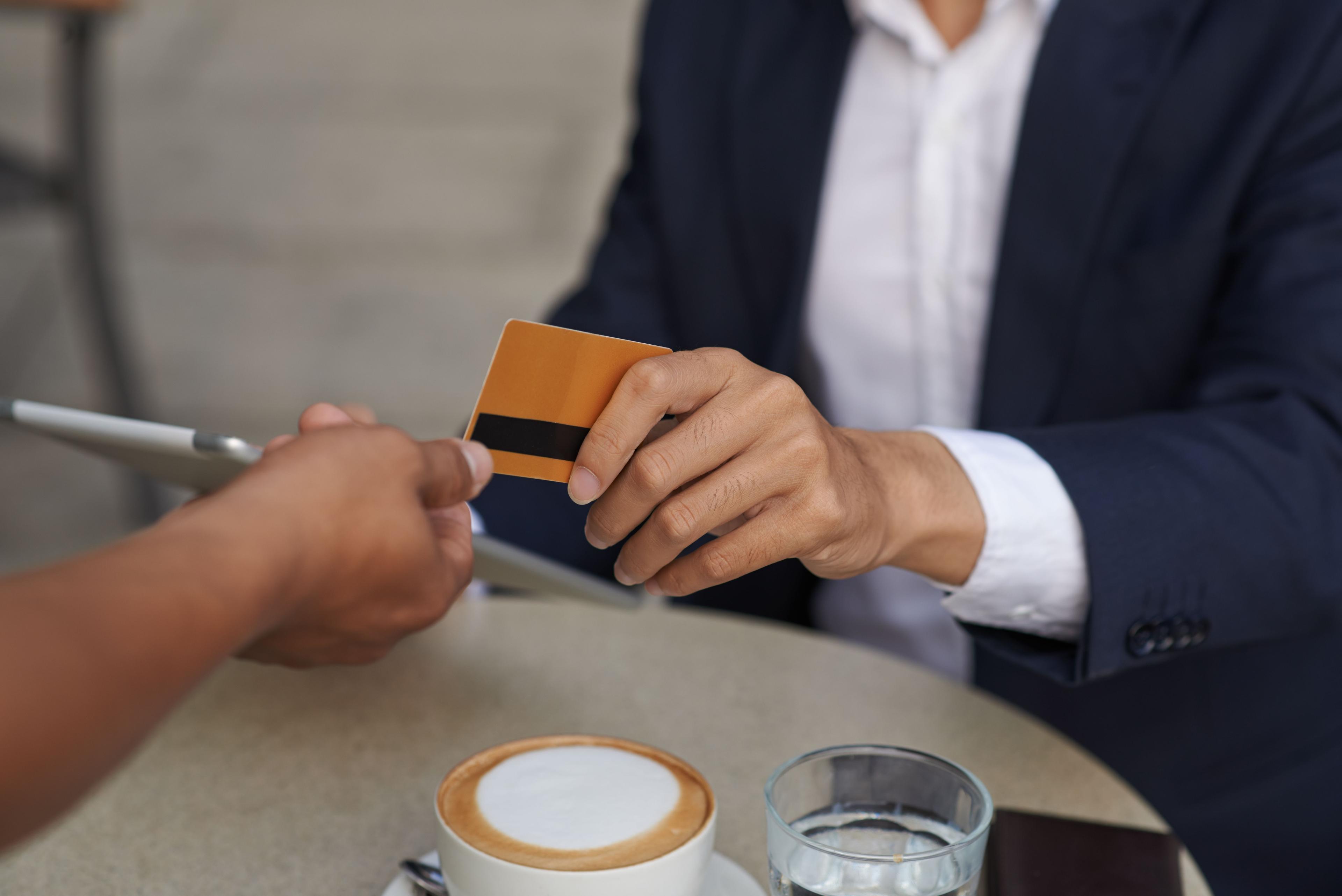 Business professional handing an orange payment card to another person at a café table.