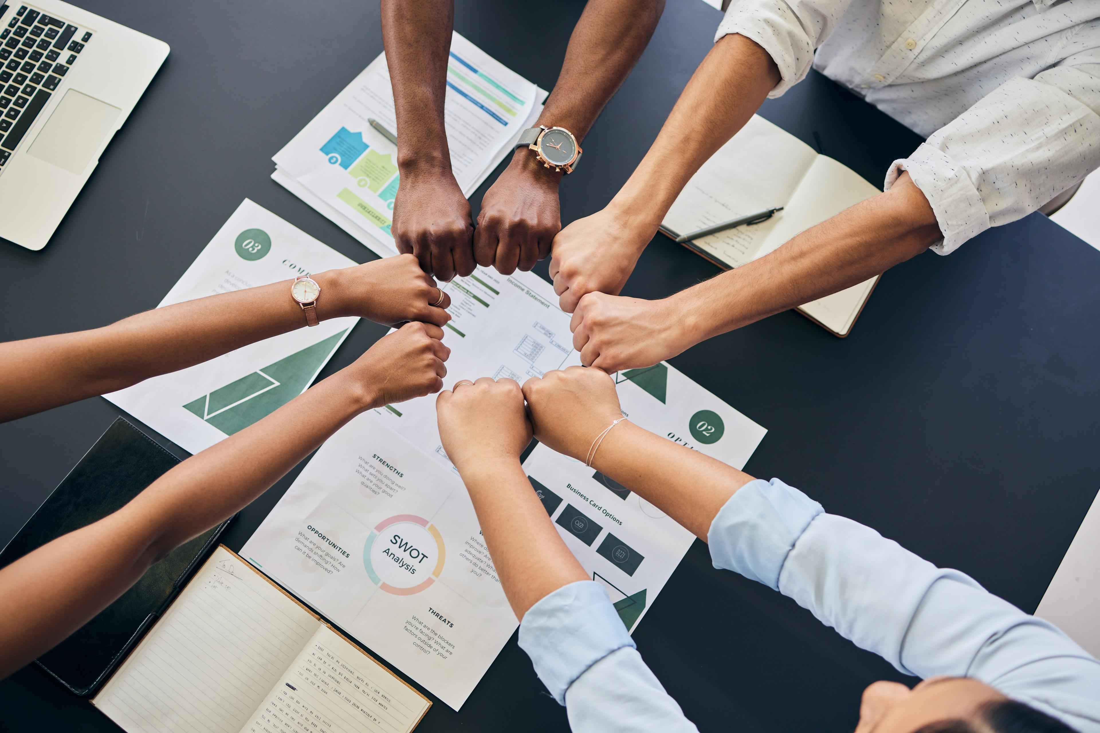 Coworkers joining their fists together over a table with business reports and charts.