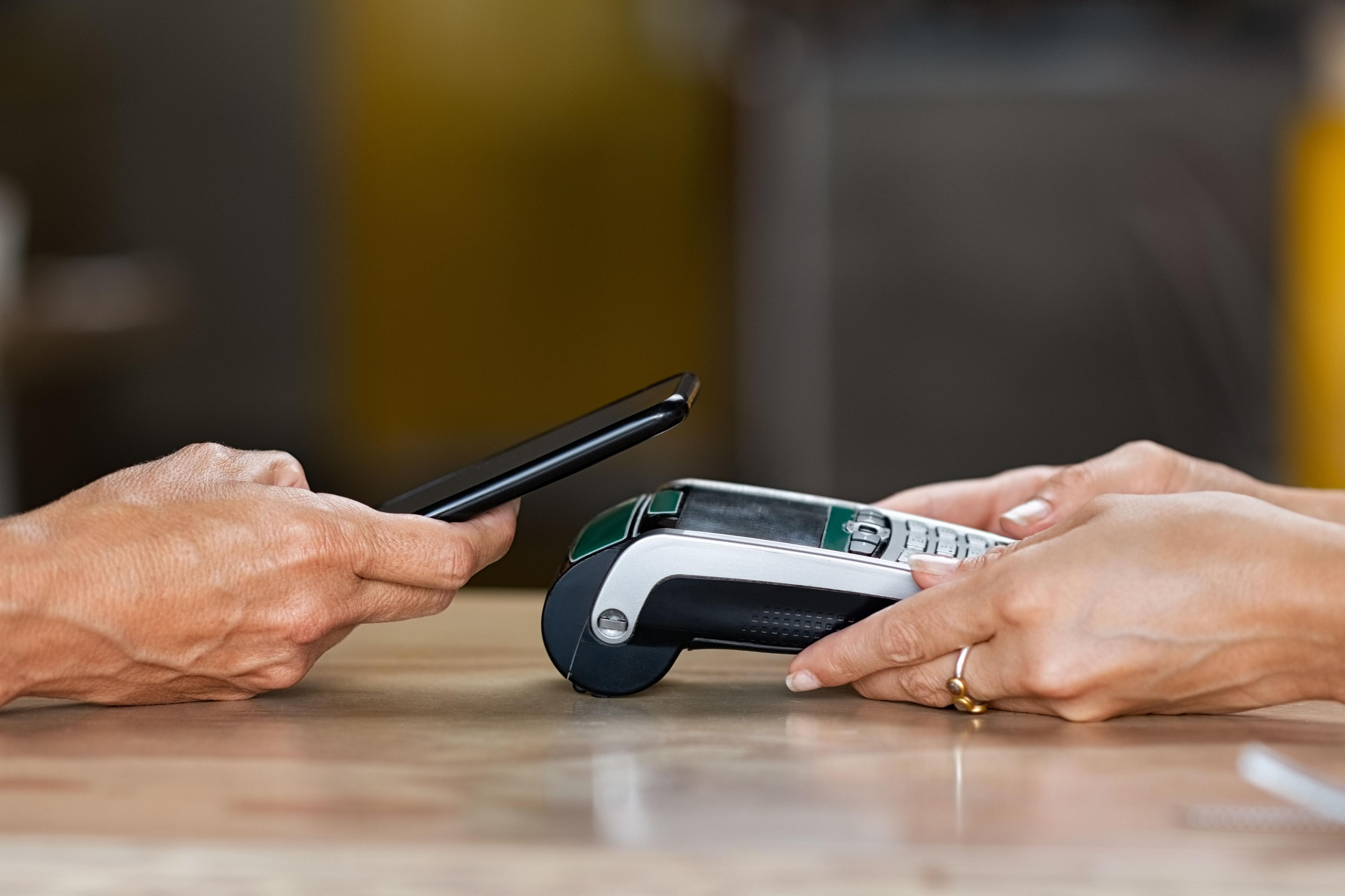 Customer making a contactless mobile payment with a smartphone at a card terminal.