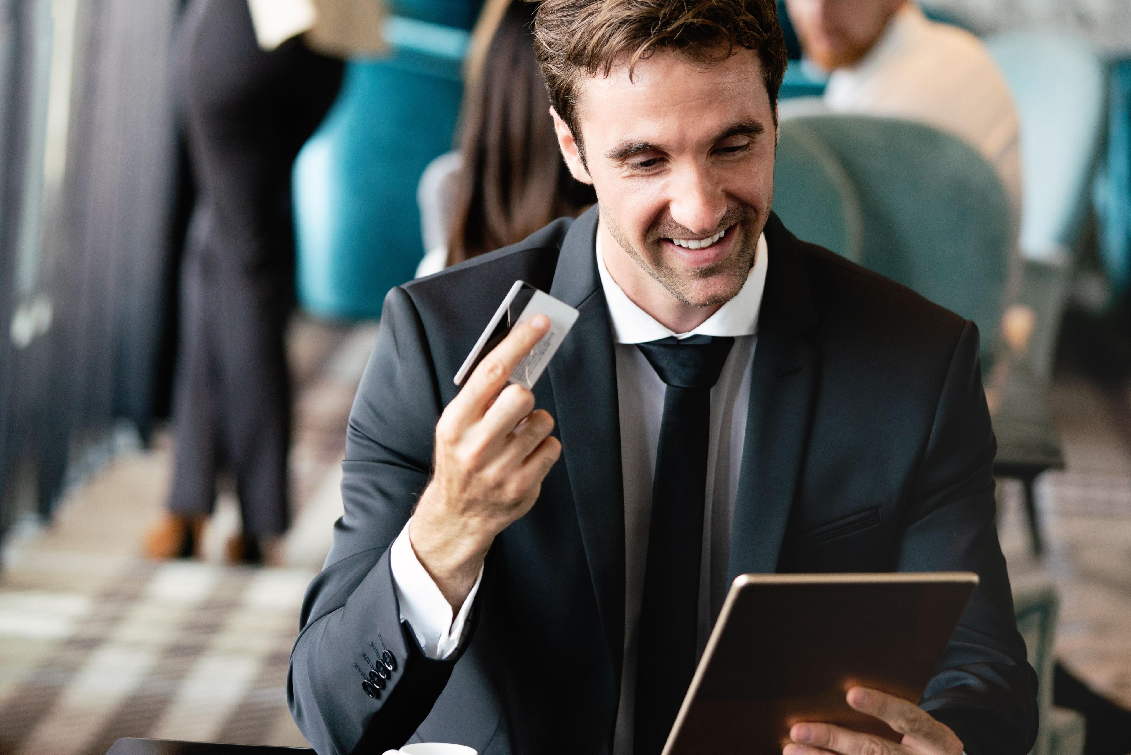 Businessman holding a payment card while smiling at a tablet.