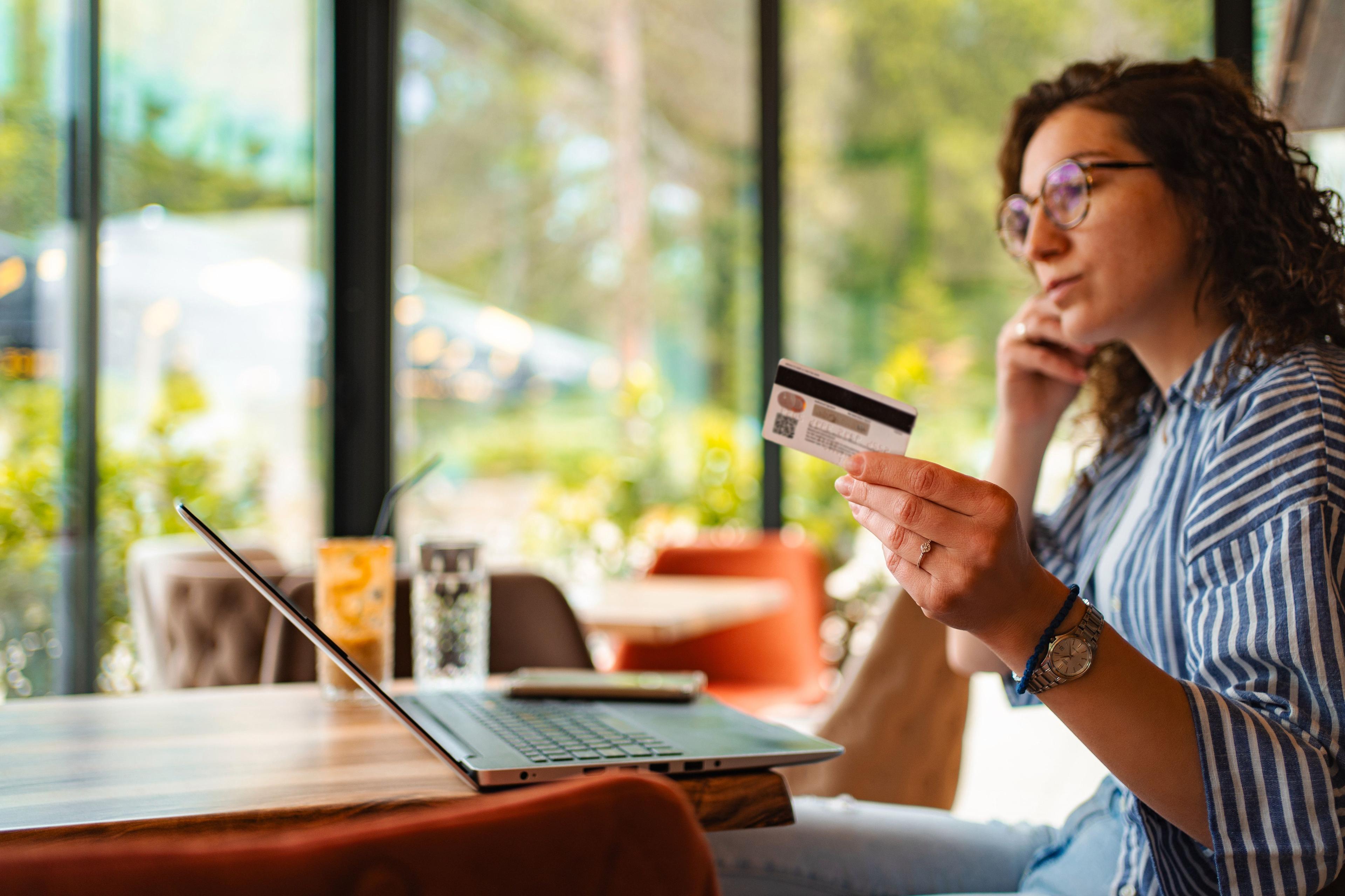 Woman holding a payment card while using a laptop at a café.
