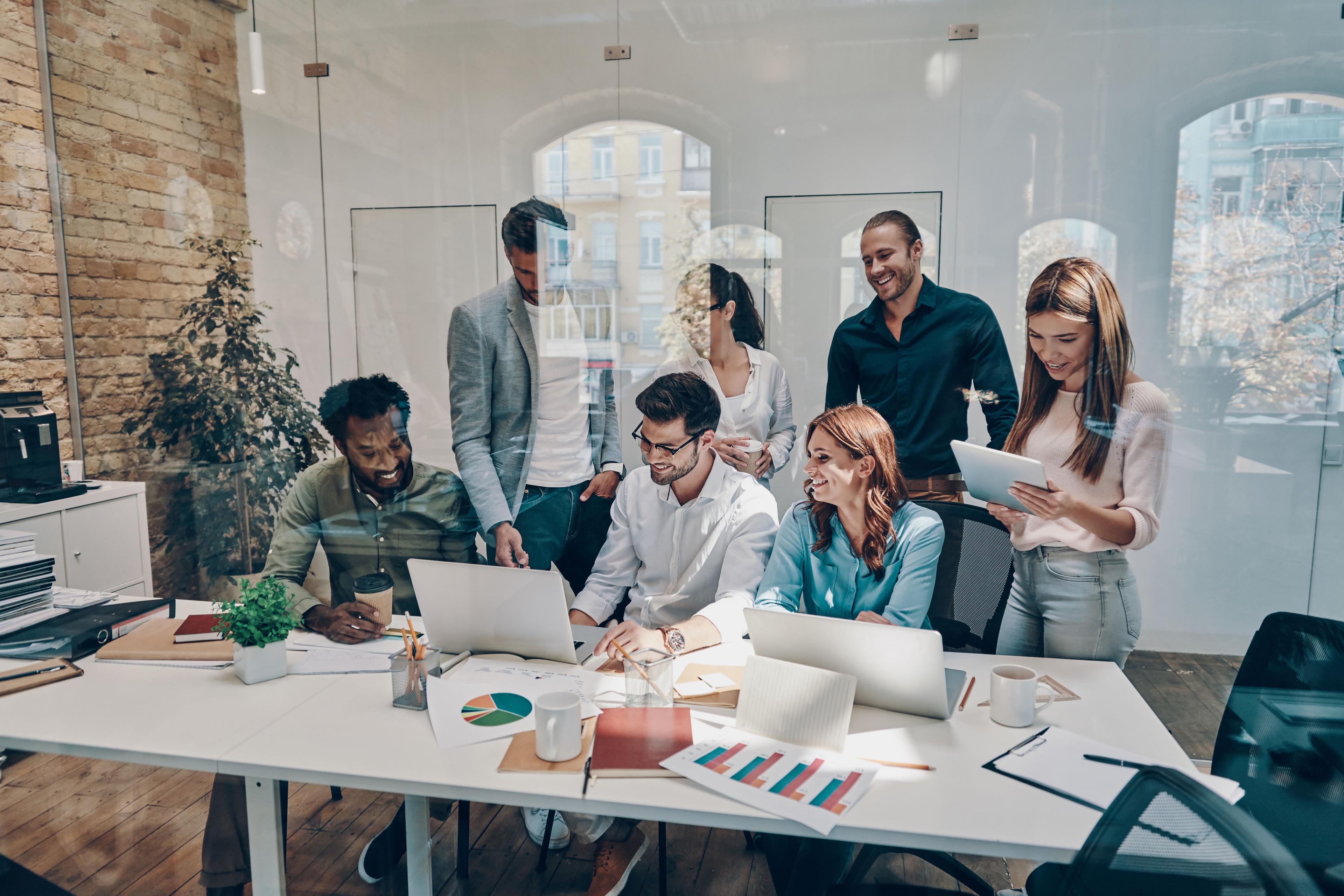 Team of coworkers collaborating around a table with laptops, documents, and charts in a modern office.