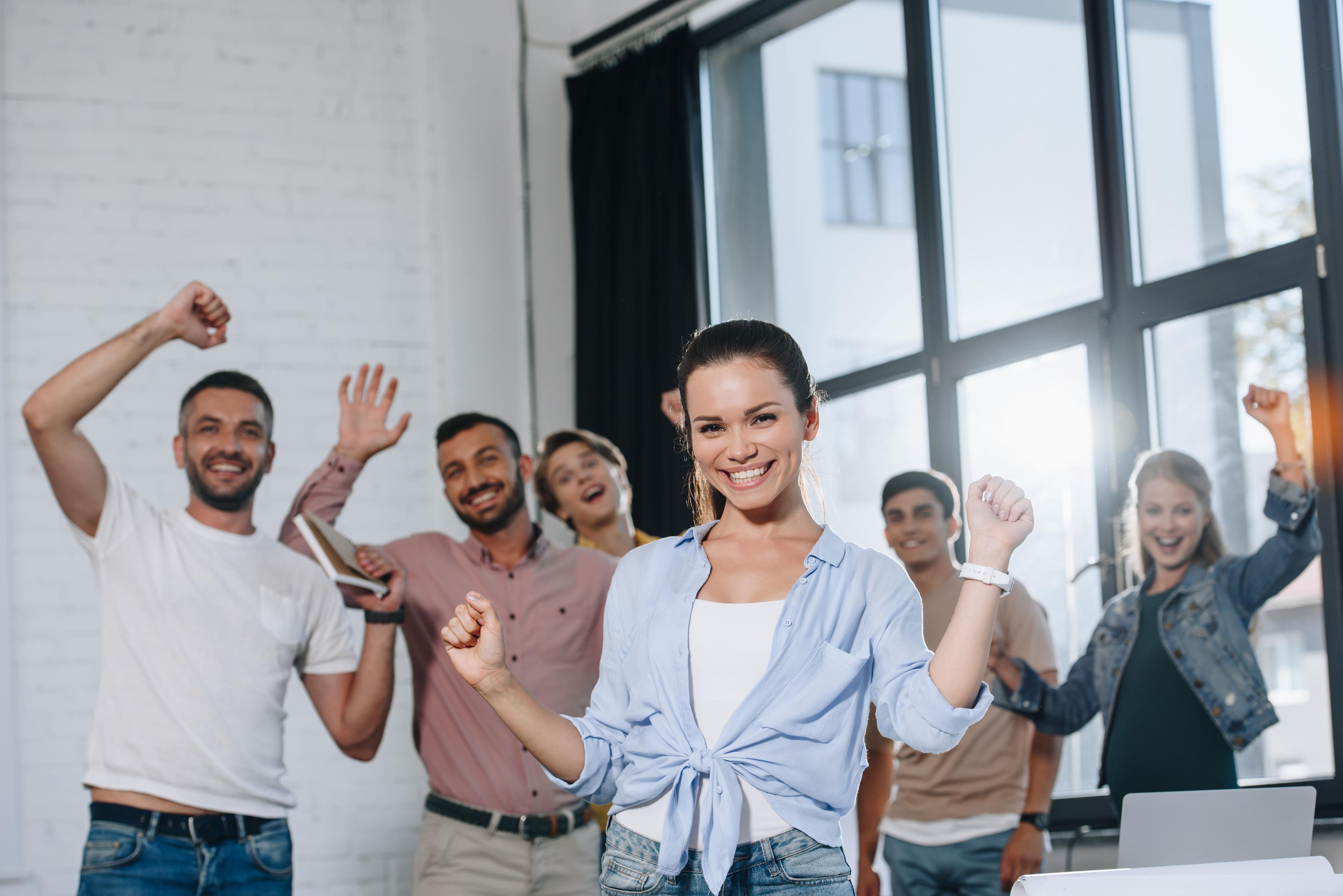 Smiling employee celebrating with a group of cheering coworkers in a bright office.